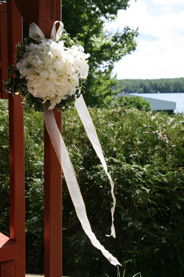 White flowers and ribbon tied to a wooden railing beside a lake