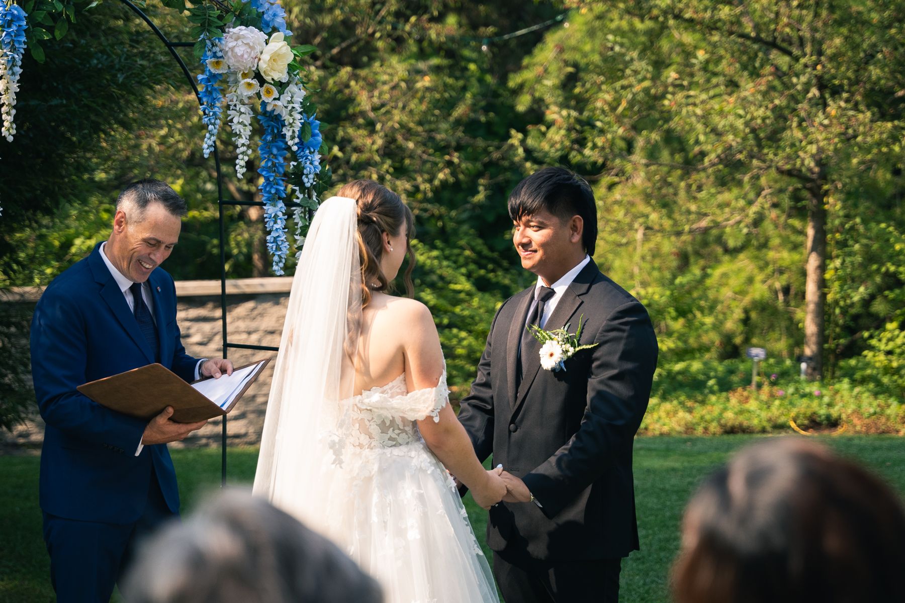 Lindsay officiating a garden ceremony as the couple hold hands under a floral arch