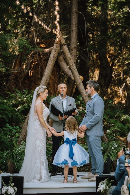 Lindsay officiating a forest ceremony as the couple hold hands with their young daughter between them